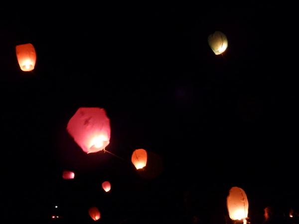 真っ暗な中、薄いピンク、薄いオレンジ、薄いグリーンのフライングキャンドルを下から見た写真